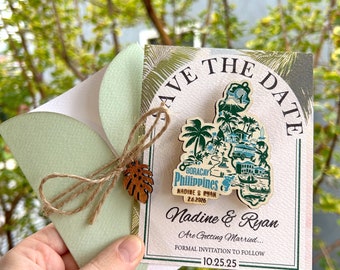 Puede incluir: Una tarjeta de guardar la fecha con un mapa de madera de Boracay, Filipinas. La tarjeta está decorada con hojas tropicales verdes y marrones y el texto "Save the Date" en un círculo dorado. El texto "Nadine & Ryan Are Getting Married... Formal Invitation to Follow 10.25.25" está impreso en la tarjeta.