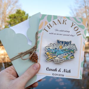 Può includere: Biglietto di ringraziamento con un motivo astratto verde e bianco. Il biglietto presenta un ritaglio in legno di Newport, Rhode Island, con il testo "Carrah & Nick 10.09.2026" stampato su di esso. Il biglietto ha anche il testo "Grazie" e "Per aver festeggiato con noi il nostro giorno speciale!" stampato su di esso.