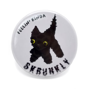 May include: A white button featuring a black cat illustration and the text "Feelin' Kinda Skrunky" in black.
