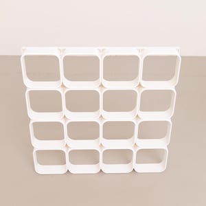 Può includere: Un'unità di stoccaggio modulare bianca con sedici aperture quadrate disposte in quattro file da quattro. L'unità è realizzata in un materiale liscio e solido ed è progettata per essere montata a parete o indipendente. Il design è minimalista e moderno.