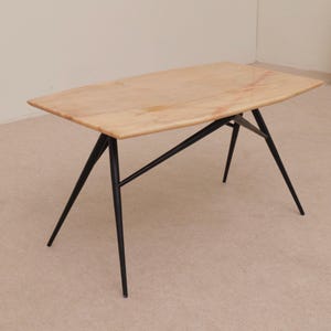 Peut inclure: Une table rectangulaire avec un plateau en bois clair et des pieds en métal noir. La table a un design moderne du milieu du siècle, avec une esthétique épurée et minimaliste. Les pieds sont inclinés et offrent une base solide. La table mesure environ 122 cm de long.