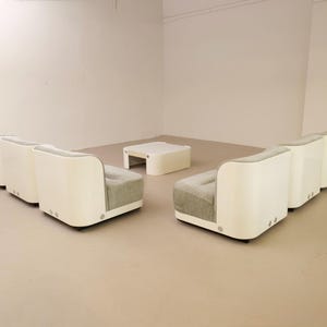 May include: A modern living room set featuring a white sofa with rounded edges and gray upholstered cushions. A matching white square coffee table sits in the center. The furniture is arranged in a spacious, well-lit room.