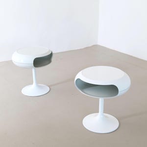 Peut inclure: Deux tables d'appoint blanches au design moderne et unique. Chaque table présente un plateau rond avec une découpe incurvée et un pied unique et fin. Les tables sont placées sur un fond neutre, soulignant leur esthétique minimaliste.