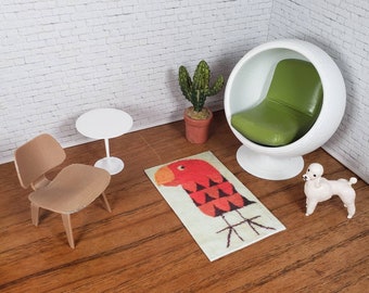 May include: Miniature mid-century modern dollhouse furniture set. Includes a white round table, a tan chair, a white ball chair with a green cushion, a rug with a red parrot design, a cactus, and a white poodle figurine.