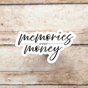 May include: White sticker with black text that reads "memories over money".