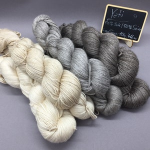 Könnte beinhalten: Vier Knäuel Garn in den Farben Weiß, Grau und Braun. Das Garn ist mit "Yetti 50% Yak/50% Seide Laufmenge: 100g/466m" beschriftet.