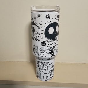 May include: White insulated tumbler with black illustrations of characters and scenes from The Nightmare Before Christmas. The tumbler has a clear lid and the words "What's This?" in a stylized font.