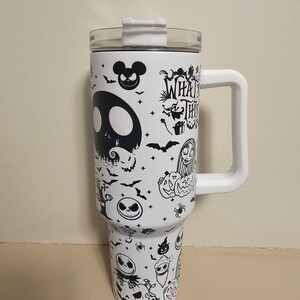 May include: White travel mug with a clear lid and white handle. The mug is decorated with black illustrations of characters and imagery from "The Nightmare Before Christmas", including Jack Skellington and the text "What's This?"