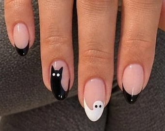 May include: Nail art featuring a nude base with black French tips on the outer nails. The middle nails display a black cat silhouette with white eyes on one finger and a white ghost figure with black eyes on the other, creating a themed manicure.