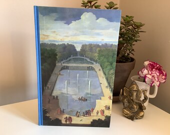 May include: A hardcover book with a blue spine and a landscape painting on the cover. The painting depicts a formal garden with a large fountain, trees, and people. The sky is blue with white clouds.