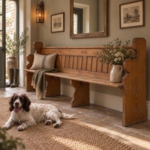 May include: A long, wooden church-style bench with a high back and curved side supports. The bench features a light brown wood grain finish, a beige throw pillow with a dark stripe, a green knit blanket, and a ceramic pitcher with greenery.