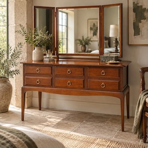May include: A wooden vanity table featuring a tri-fold mirror and six drawers with circular brass ring pulls. The piece has a warm brown finish, a rectangular top, and four tapered legs. It is positioned as a standalone furniture item.