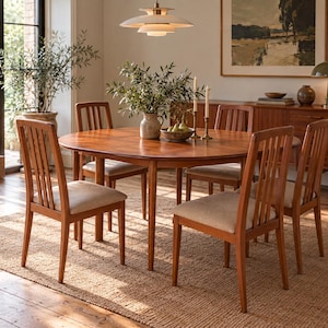 May include: A round wooden dining table with four matching chairs featuring vertical slat backs and beige upholstered seats. The table surface is smooth and brown, centred with a ceramic vase containing green branches and a bowl of pears.