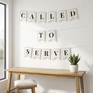 Puede incluir: Una pancarta decorativa con las palabras "CALLED TO SERVE" en letras negras sobre banderines blancos. Debajo, un escritorio de madera clara con una pequeña planta en maceta. Todo colgado en una pared blanca.