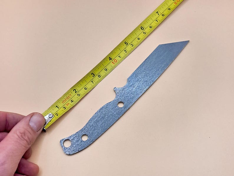 May include: A silver knife blank with a textured finish, measuring approximately 18 cm in length. The knife blank is being measured with a yellow tape measure.