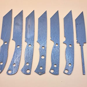 May include: Eight metal knife blanks with different shapes and sizes. The blanks are all made of a silver-coloured metal and have a rough, unfinished surface.