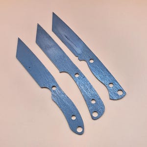May include: Three unfinished metal knife blades with a brushed finish. The blades are different sizes and shapes.