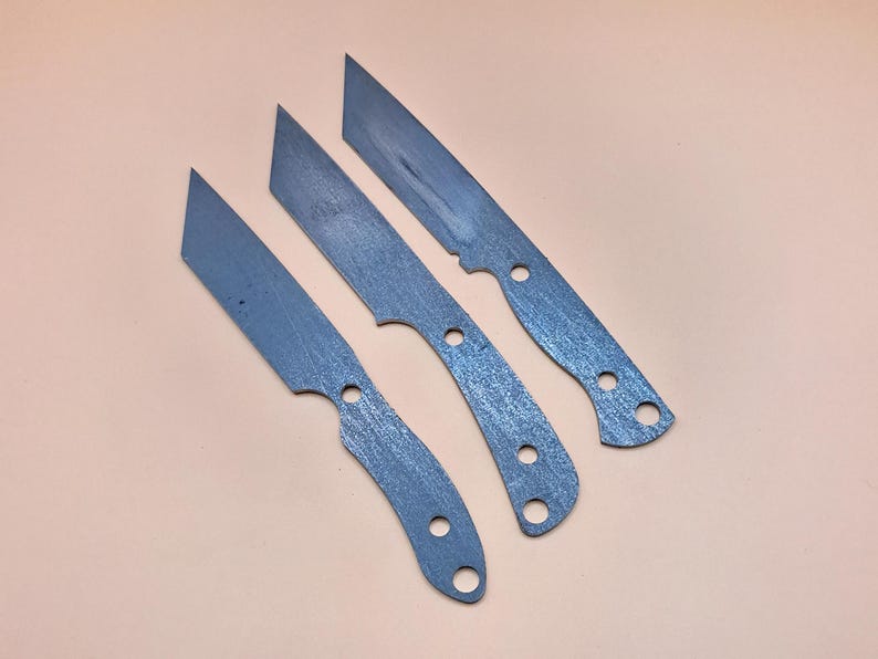 May include: Three unfinished metal knife blades with a brushed finish. The blades are different sizes and shapes.