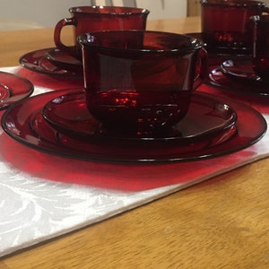 May include: Set of four red glass teacups and saucers. The cups and saucers are all the same size and shape. The cups have a rounded shape and a small handle. The saucers are round and have a slightly raised edge.