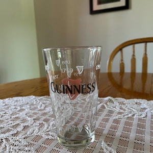 May include: A clear pint glass with the Guinness logo in red and white. The glass has the year 1759 printed on it, along with the words "Guinness and Co."