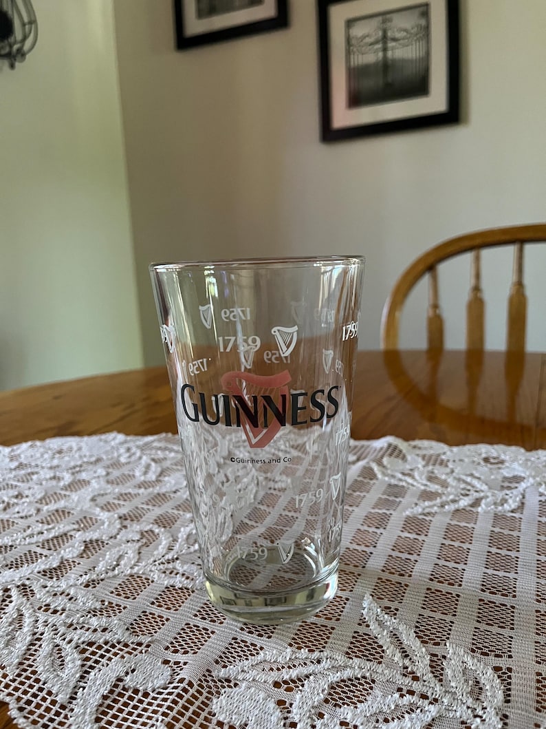 May include: A clear pint glass with the Guinness logo in red and white. The glass has the year 1759 printed on it, along with the words "Guinness and Co."