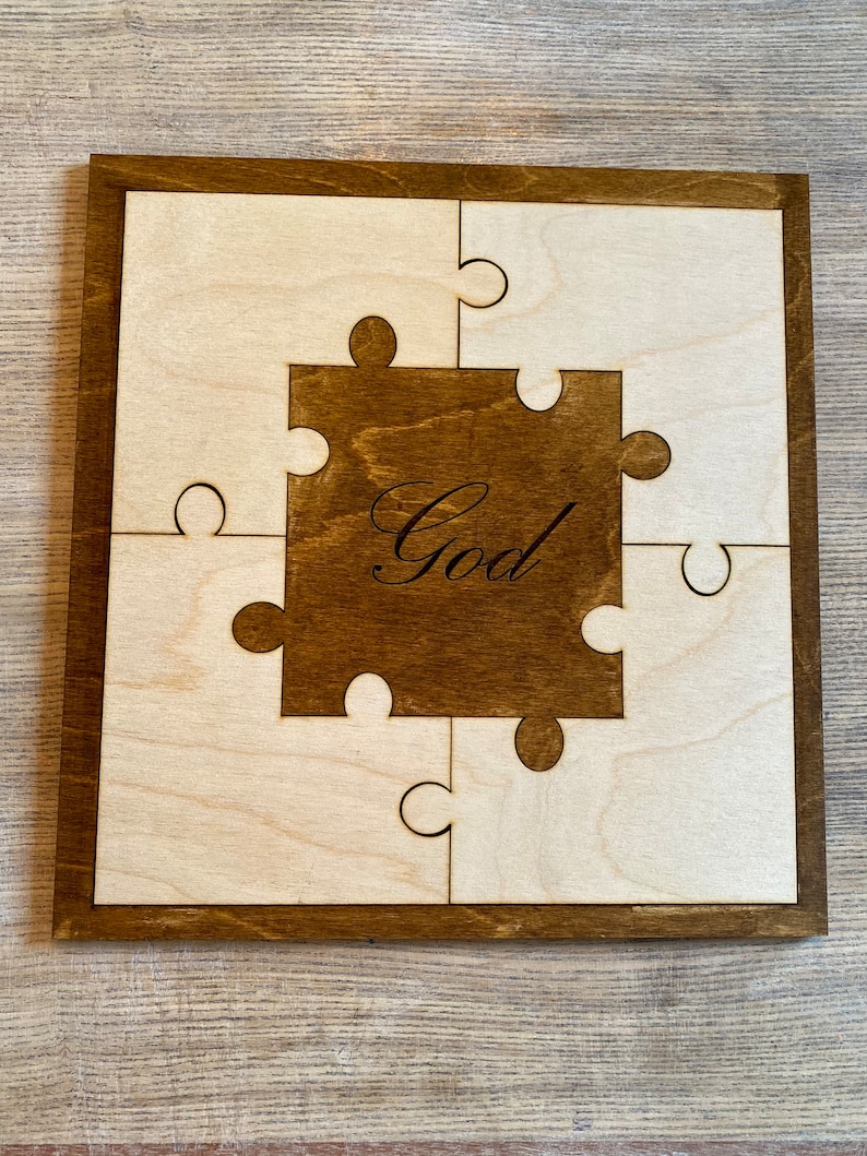 May include: Wooden puzzle with a dark brown frame and centre piece. The centre piece has the word "God" in a script font. The puzzle pieces are light wood colour. The puzzle is square in shape.