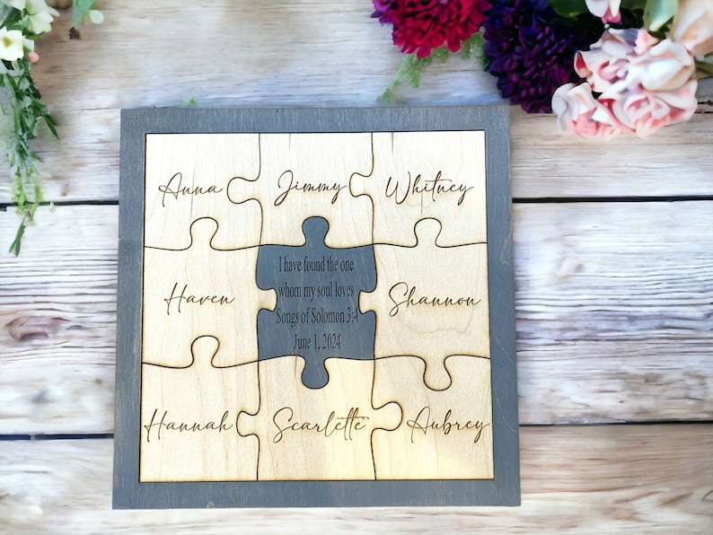 May include: A wooden jigsaw puzzle with a grey frame, featuring nine pieces. Each piece is engraved with a name. The central piece is a darker grey and has a quote and date. A unique personalised gift.