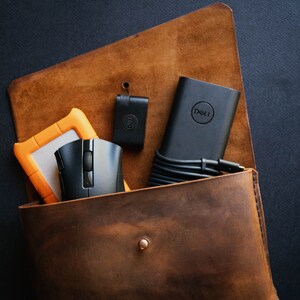 May include: A brown leather bag with a black Dell laptop charger, a black mouse, a small black device, and an orange external hard drive inside.