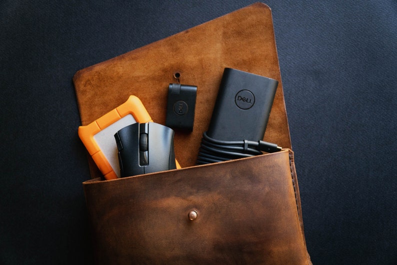 May include: A brown leather bag with a black Dell laptop charger, a black mouse, a small black device, and an orange external hard drive inside.