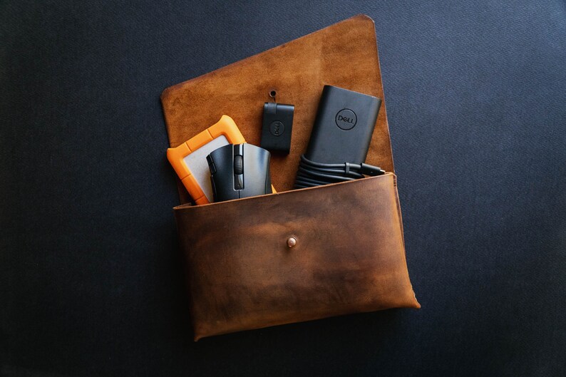 May include: A brown leather pouch with a snap closure, containing a black mouse, a black Dell power adapter, a black USB drive, and an orange external hard drive.