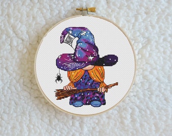 Può includere: Un gnomo viola e arancione che indossa un cappello da strega con un design a ragnatela e tiene una scopa. Il cappello ha stelle e un ragno.