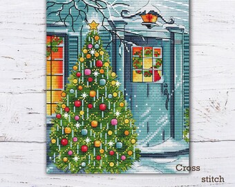 May include: Cross stitch pattern PDF of a snowy winter scene with a house and a decorated Christmas tree. The house has a blue door and a window with a wreath. The tree is decorated with colorful ornaments, lights, and a star on top.