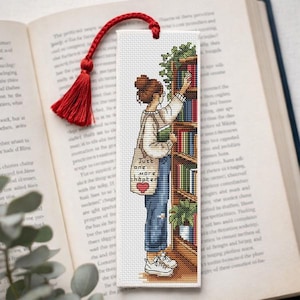 Op de afbeelding: Bladwijzer met een rode kwast, met een kruissteekontwerp van een persoon die naar een boek in een plank reikt. De persoon draagt een spijkerbroek en sneakers en draagt een draagtas met de tekst "Just one more chapter."