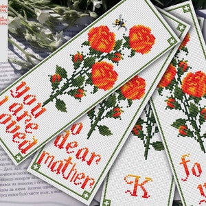 Könnte beinhalten: Vier Kreuzstich-Lesezeichen mit einem floralen Design. Die Lesezeichen zeigen einen einzelnen Stiel mit orangefarbenen Rosen mit grünen Blättern und einer Biene. Der Text auf den Lesezeichen lautet "You are loved", "Dear Mother", "K" und "For you".