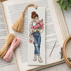 Op de afbeelding: Kruissteek bladwijzer met een vrouw die een boek leest en bloemen vasthoudt. De bladwijzer heeft een kwast en de tekst "Just one more chapter". De vrouw draagt een bril, jeans en sneakers.