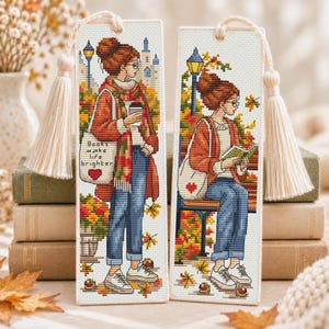 Op de afbeelding: Twee rechthoekige kruissteek bladwijzers van crèmekleurige stof met witte kwastjes. Eén toont een staand persoon met een koffiebeker en een tas met de tekst "Books make life brighter". De andere toont een zittend persoon op een bankje.