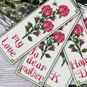 May include: Four cross-stitch bookmarks with a floral design and text. The bookmarks feature a pink rose with green leaves and stems. The text on the bookmarks reads "Love my", "To dear mother", "Happy", and "Day".