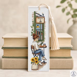May include: A rectangular cross-stitch bookmark featuring a person sitting on a chair at a small table, reading a book with a coffee cup nearby. The design includes a bookstore window with the text BOOKS & COFFEE, sunflowers, and a cream tassel.