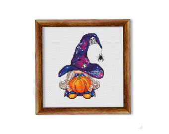 Può includere: Uno schema di punto croce di un gnomo strega che indossa un cappello viola e blu con stelle e un design a ragnatela. Lo gnomo tiene una zucca arancione.