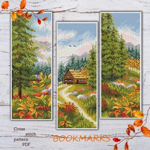 Op de afbeelding: Drie kruissteek-bladwijzerpatronen met een hut in het bos met herfstbladeren. De patronen zijn gemarkeerd met "BOOKMARKS" en zijn beschikbaar als PDF-downloads.