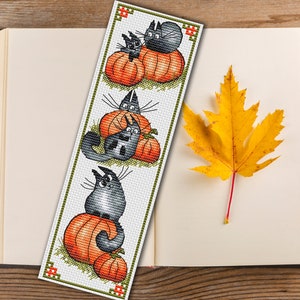 May include: A cross-stitch bookmark featuring three black cats with orange pumpkins. The bookmark is white with green accents.