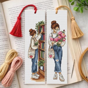 Puede incluir: Dos marcapáginas de punto de cruz. Cada uno representa a una persona con moño, gafas y vaqueros. Uno alcanza un libro, el otro sostiene un libro y flores. Tienen bolsas con "Just one more chapter".