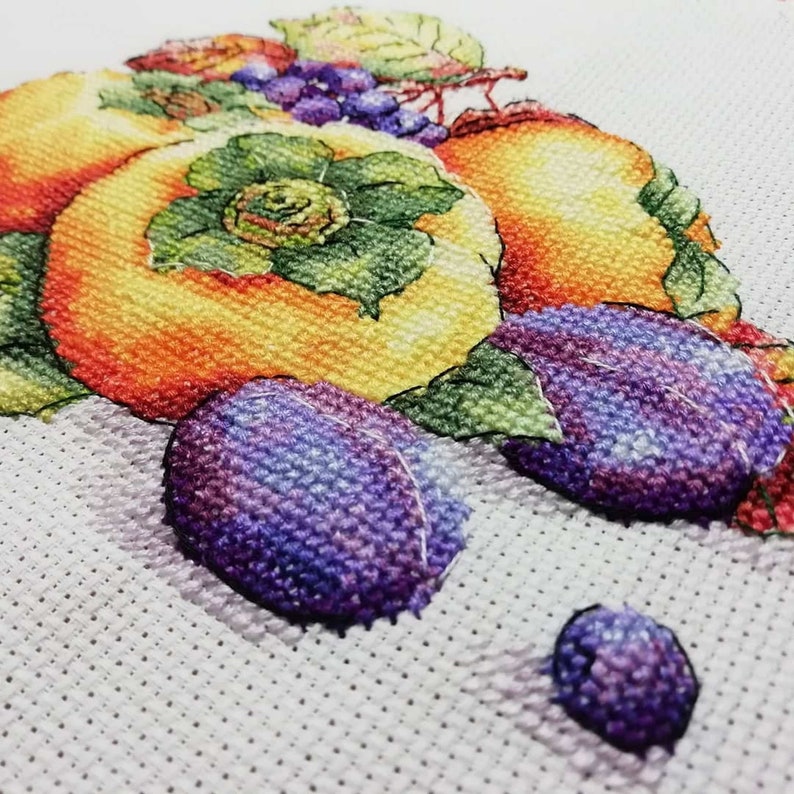 Puede incluir: Bordado de punto de cruz de un bodeg&oacute;n con un grupo de frutas, incluyendo melocotones, ciruelas y uvas. La fruta se representa en un estilo realista con colores vibrantes y detalles intrincados.