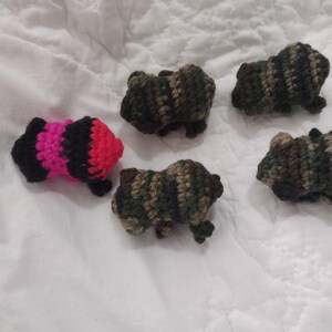May include: Five handmade crochet animal figurines. Four are in camouflage colors of green, brown, and black. One is pink, black, and red. The figurines are small and appear to be lying on a white surface.