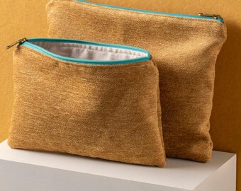 Puede incluir: Dos estuches de tela de color amarillo mostaza con tiradores de cremallera de color turquesa. Los estuches están anidados uno dentro del otro, con el estuche más pequeño en la parte delantera.
