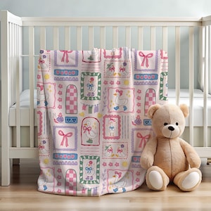May include: A light pink blanket featuring a repeating pattern of white ducks wearing blue boots and pink bows, interspersed with pink bows, small yellow suns, purple snails, and checkered arches, all framed within colorful rectangular borders.