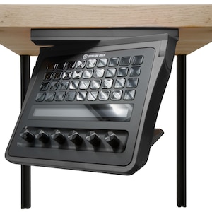 May include: A black Stream Deck control console mounted underneath a light wood surface. The device features a grid of thirty-two square LCD keys, a horizontal touch strip, and five circular rotary dials along the bottom edge of the frame.