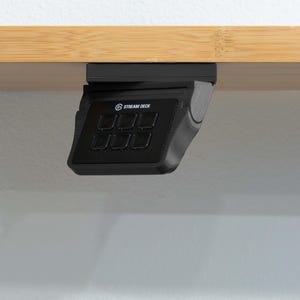 Może przedstawiać: Czarny kontroler Stream Deck mini z 6 przyciskami zamontowany pod drewnianą półką.