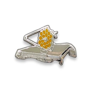May include: A silver pin depicting a stylized image of a space telescope with a hexagonal mirror. The mirror is yellow and the rest of the telescope is silver.