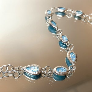 May include: A silver chain bracelet with teardrop-shaped blue stones. The stones have a textured, iridescent finish.